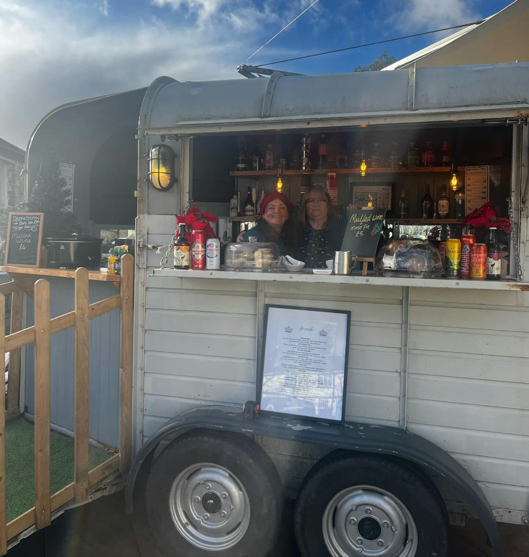 Two of the Y Bocs Jin team smiling behind the horsebox bar at a winter event